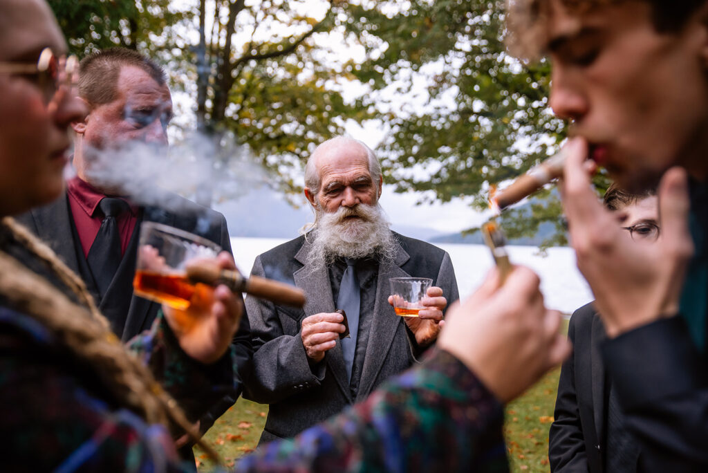 Grandpa watches as bride and brides man light and smoke cigars together
