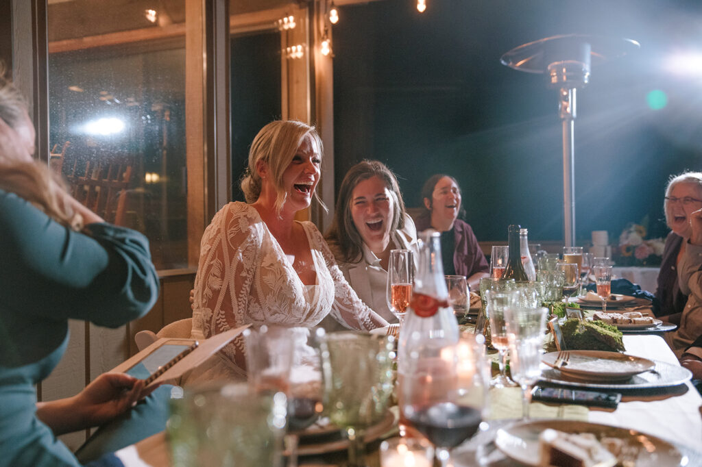 The brides laugh together during parent speeches at their wedding