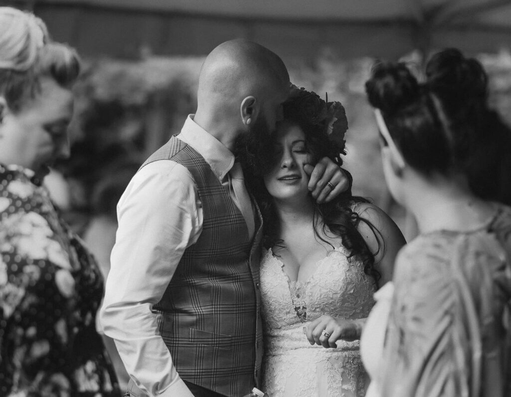 Groom pulls in bride and kisses her forehead during cocktail hour