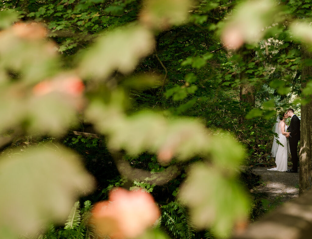 Wedding couple under a tree kissing photographed through the maple leaves