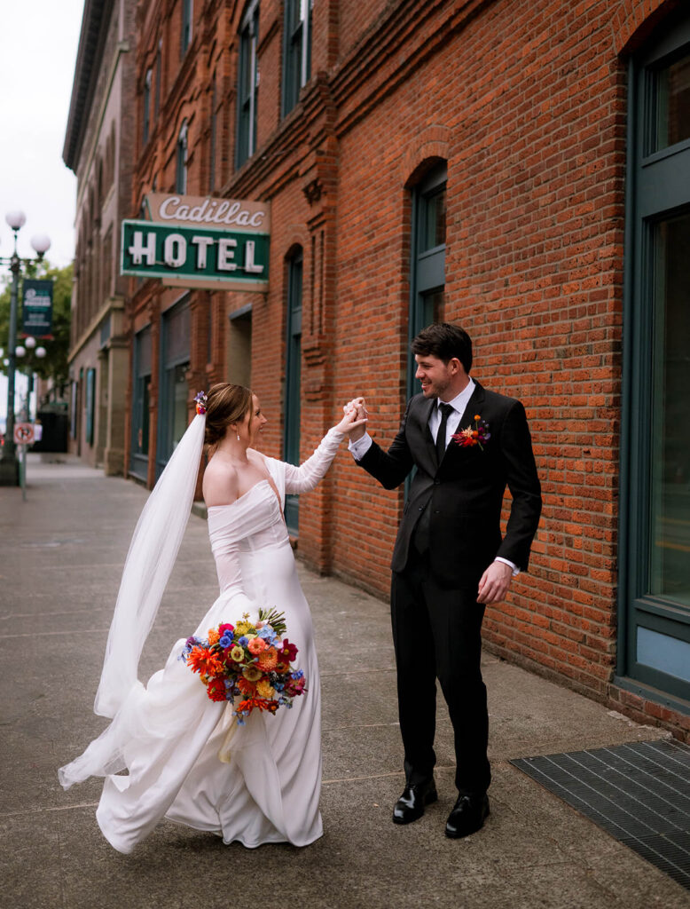 Bride and groom dance and play in front of Cadillac Hotel in Pioneer Square on wedding day